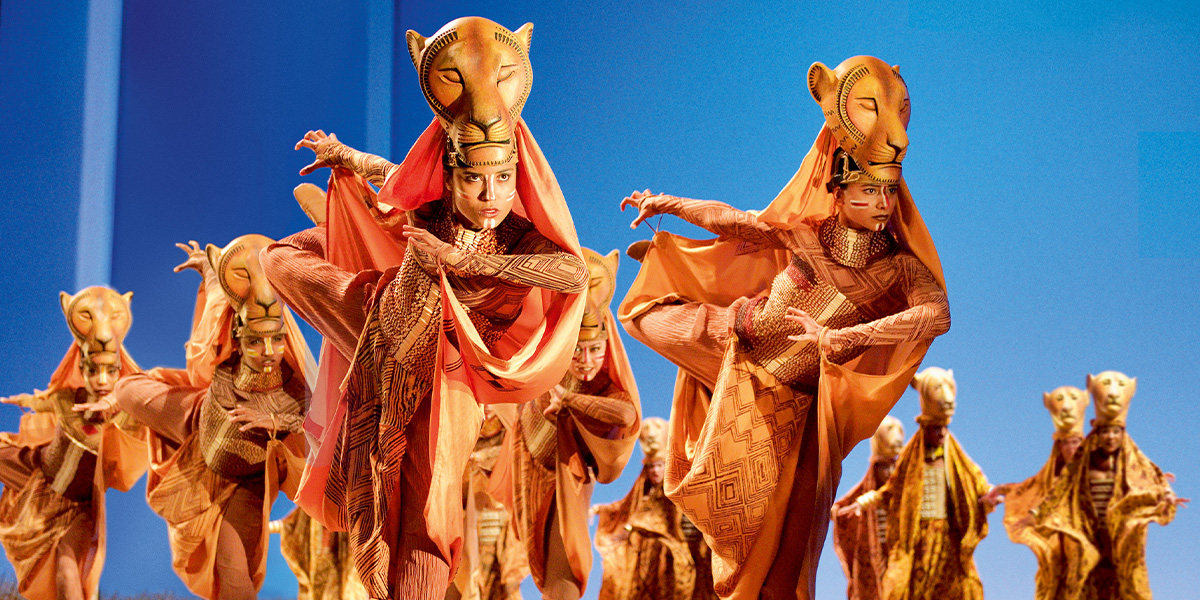 A lioness stealthily stalks through tall grass, showcasing her tawny fur against a vibrant green background.