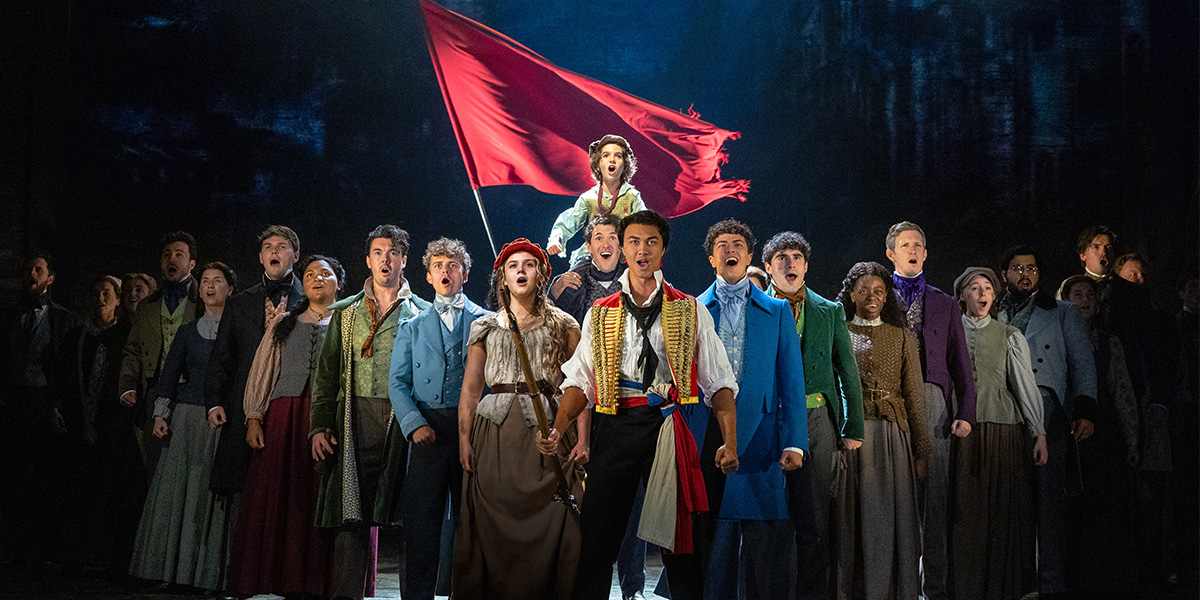 A dramatic scene from Les Misérables featuring actors in period costumes, with a dark, moody background.