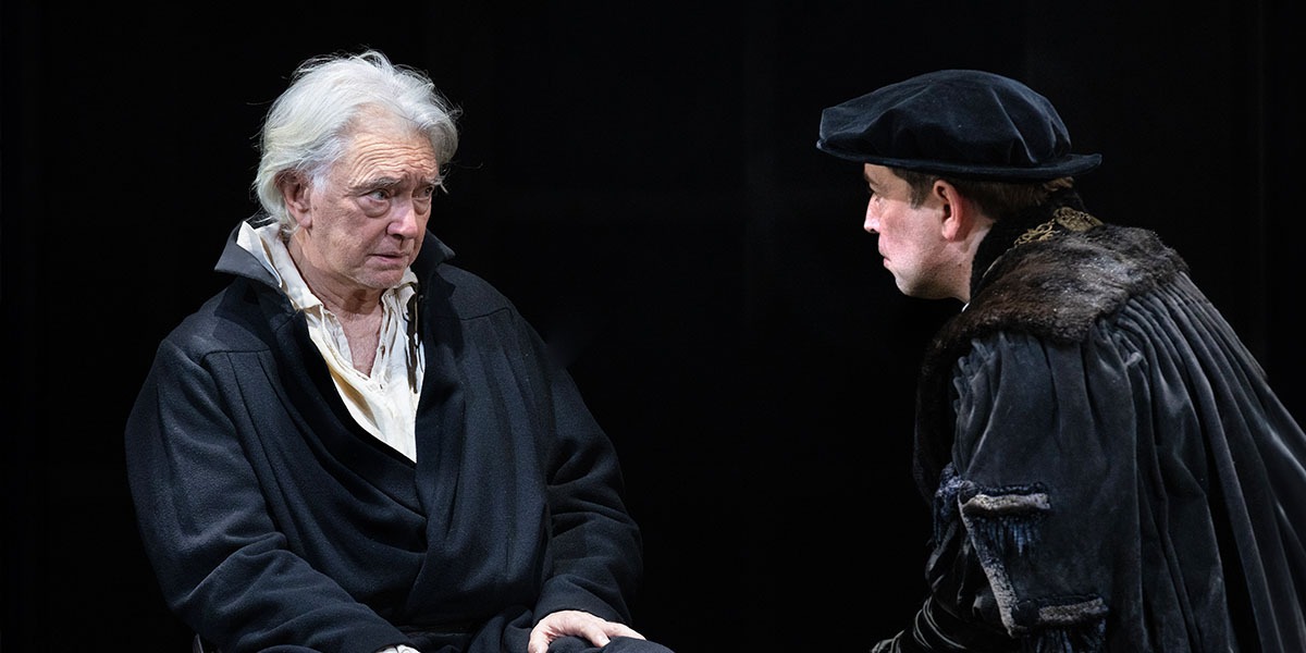 Martin Shaw and Edward Bennett are talking to each other, sat down, in Tudor dress