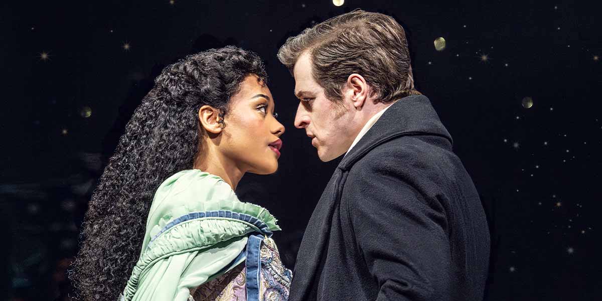 Beatrice Penny-Touré as Christine Daaé and Ashley Gilmour as Raoul face each other intensely against a dark background.