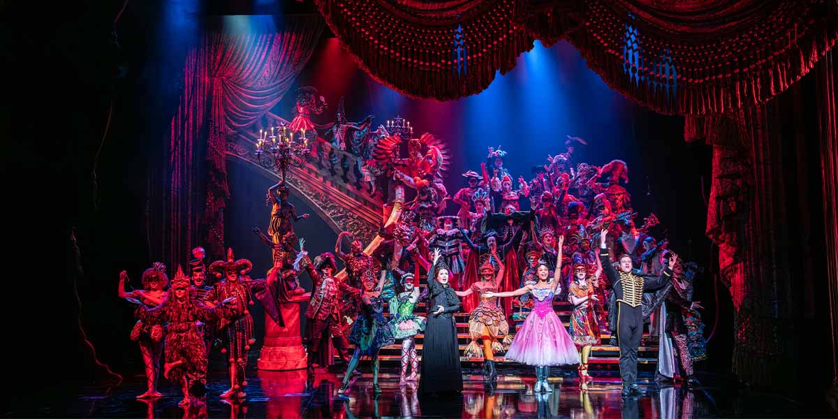 The Company performs in elaborate masquerade costumes, featuring vibrant colours and intricate designs on stage.