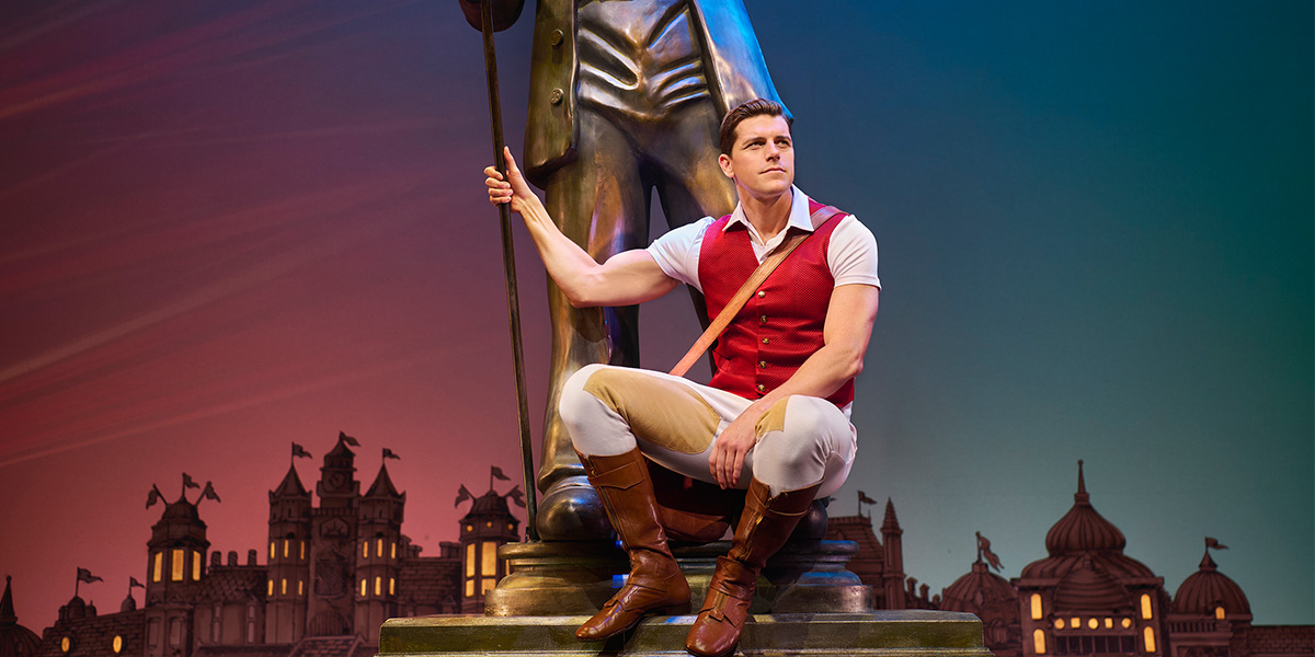 Jordan Litz as Fiyero in a green costume, performing on stage with dramatic lighting and a dark background.