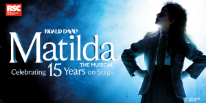 Matilda stands centre stage, surrounded by classmates, all in colourful costumes, with a vibrant backdrop.