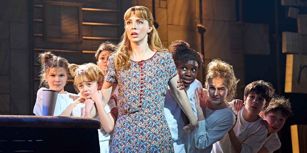 A person in a floral dress stands central as children stand behind.