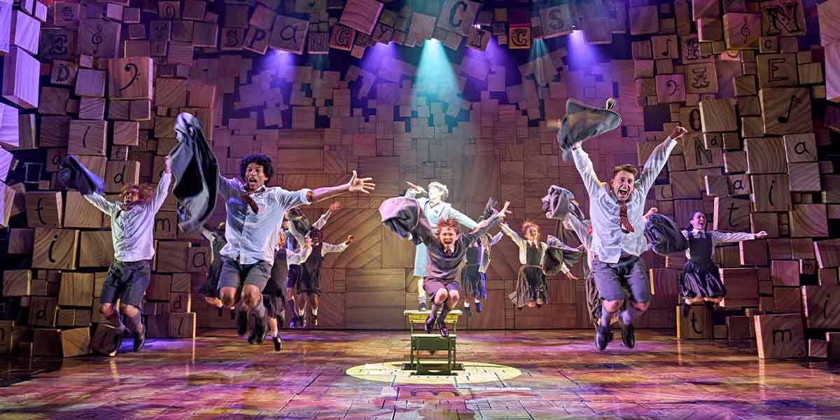 A group of children jump on a vibrant, colourful stage setting.