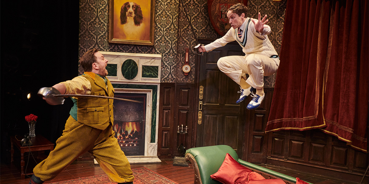 A chaotic scene from "The Play That Goes Wrong" featuring actors in disarray on stage, with props scattered.