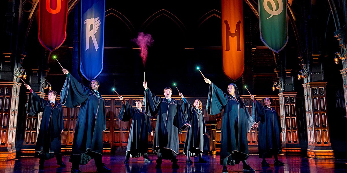 The cast of Harry Potter and the Cursed Child poses together, wearing costumes, against a theatrical backdrop.