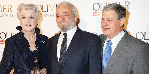 Three men pose together, smiling, holding an award at the Olivier Awards event backdrop.