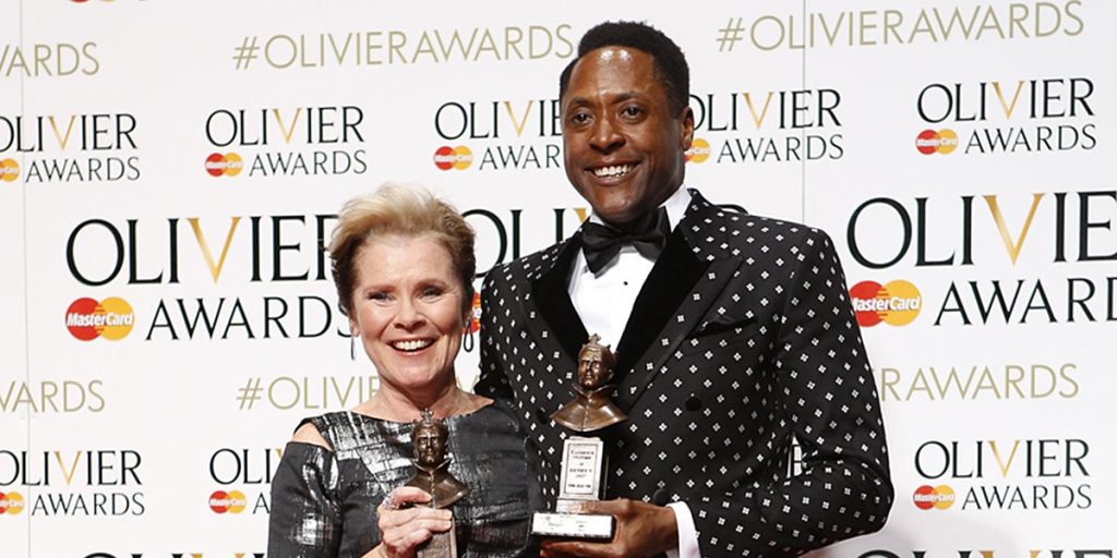 Imelda Staunton and Matt Henry hold awards, smiling against a backdrop featuring the Olivier Awards logo.