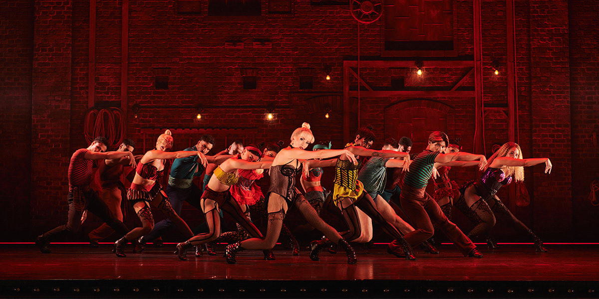 A vibrant stage scene from Moulin Rouge! featuring performers in elaborate costumes, with dramatic lighting and rich colours.