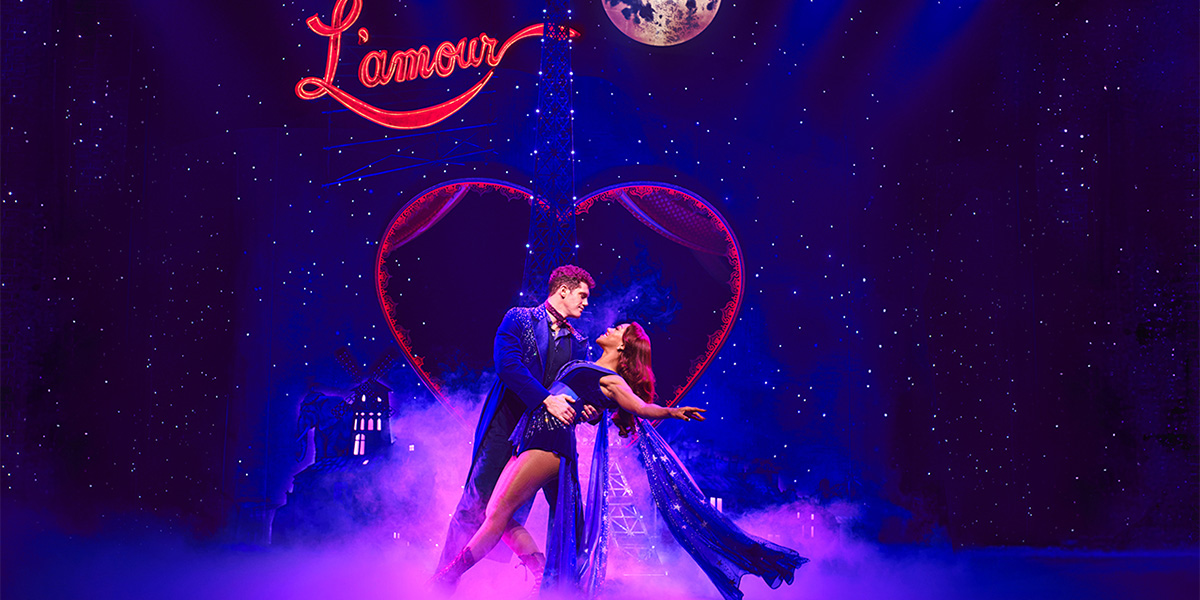 Alistair Brammer and Karis Anderson perform in vibrant costumes on stage during Moulin Rouge! The Musical.