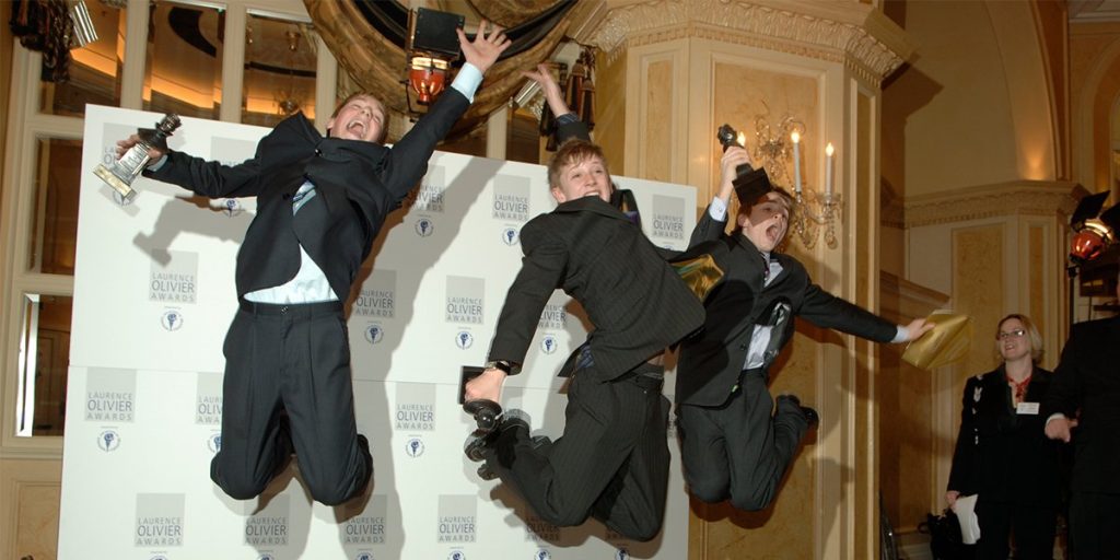 Three men in suits joyfully jump in mid-air, celebrating at the Olivier Awards 2006 event.