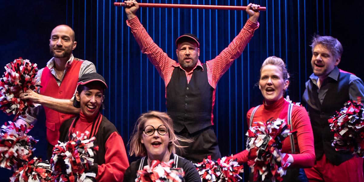 A group of performers in colourful costumes are singing energetically on stage during a musical performance.