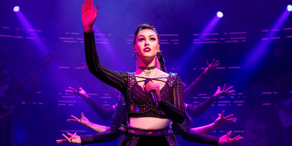 Caitlyn De Kuyper as Katherine Howard in a vibrant costume, striking a dramatic pose against a colourful backdrop.