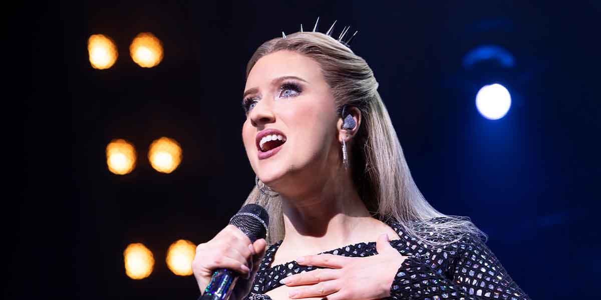 Jessica Aubrey as Jane Seymour sings passionately, wearing a sparkly black outfit, under bright stage lights.