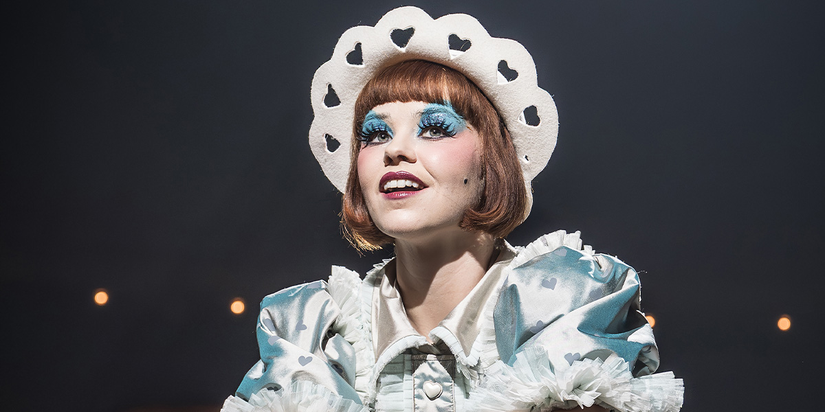 Katie Hall as Sally Bowles, wearing a sequined dress, performing on stage with dramatic lighting.