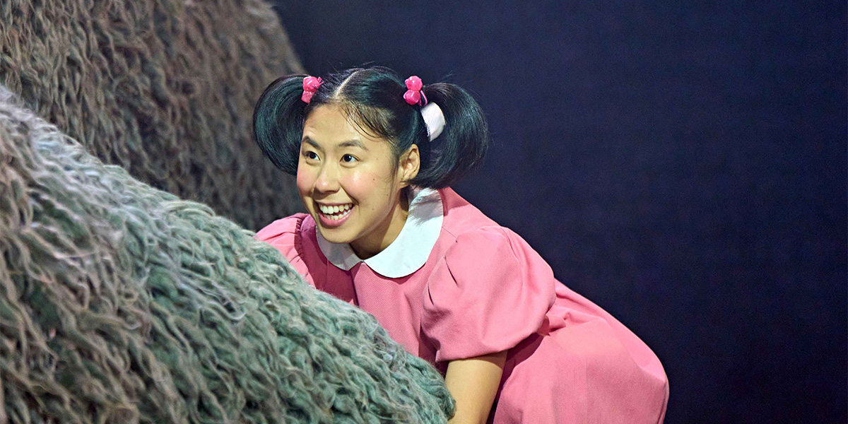 A whimsical scene featuring Totoro, a large grey creature, surrounded by lush green foliage and flowers.