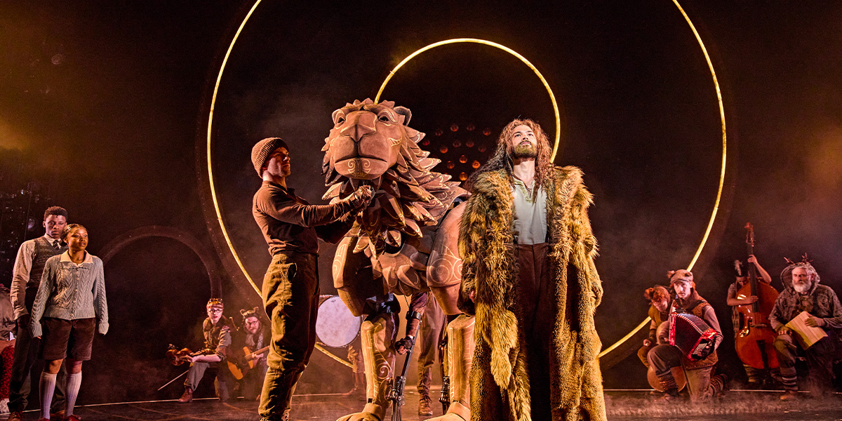 A wooden lion stands central surrounded by people.