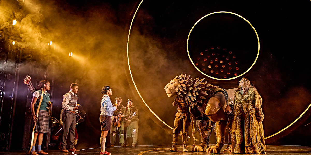 Three people can be seen speaking to a lion.