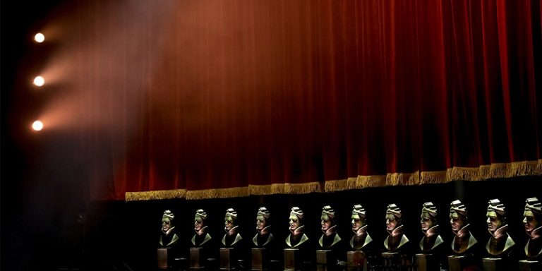 A row of busts displayed against a red velvet curtain, symbolising remembrance and tribute.