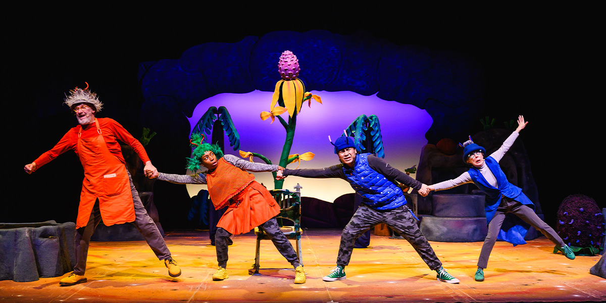 Performers in colourful costumes representing elements of nature on stage in a theatrical production.