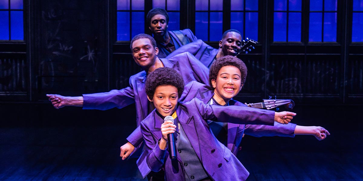 A vibrant stage scene from "MJ The Musical," featuring dancers in colourful costumes performing energetically.