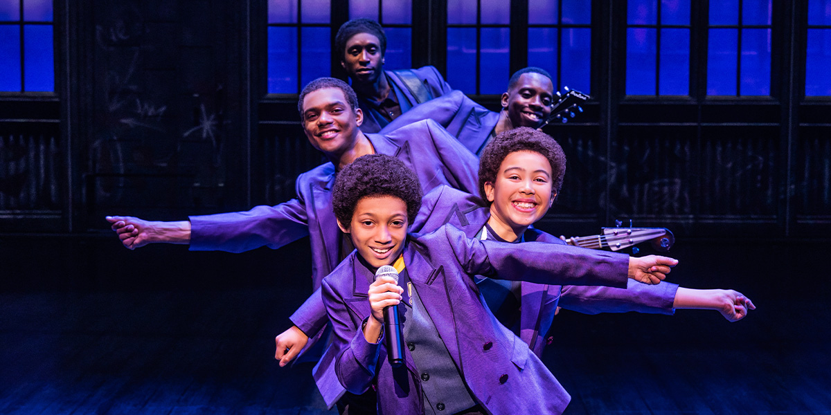 A performer in a sparkling costume dances energetically on stage, with vibrant stage lights illuminating the scene.