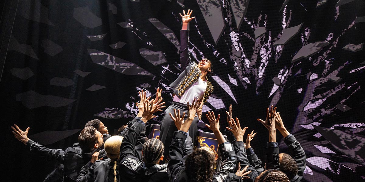 A vibrant stage scene from "MJ The Musical" featuring dancers in dynamic poses, illuminated by colourful lights.
