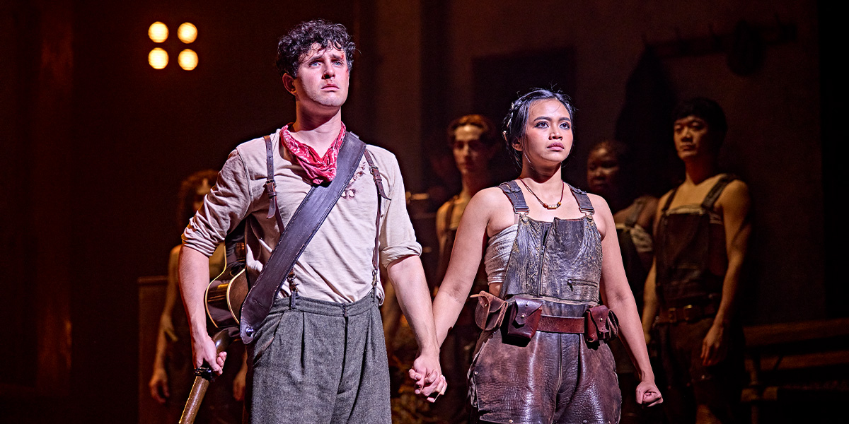 Dylan Wood and Desmonda Cathabel perform on stage, wearing elaborate costumes against a dark, atmospheric backdrop.