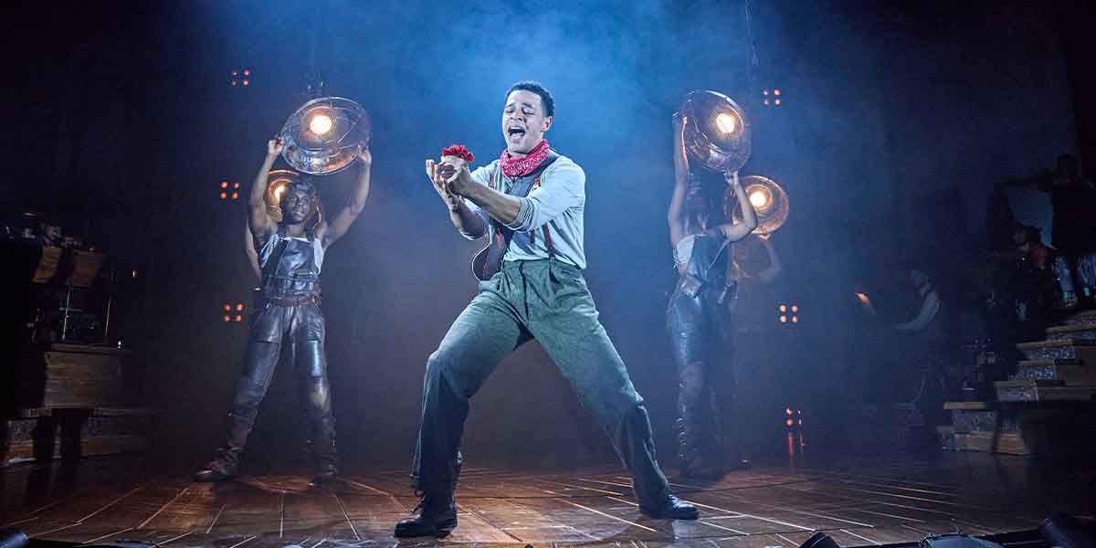 Marley Fenton performs in Hadestown, holding a rose, with two performers behind.