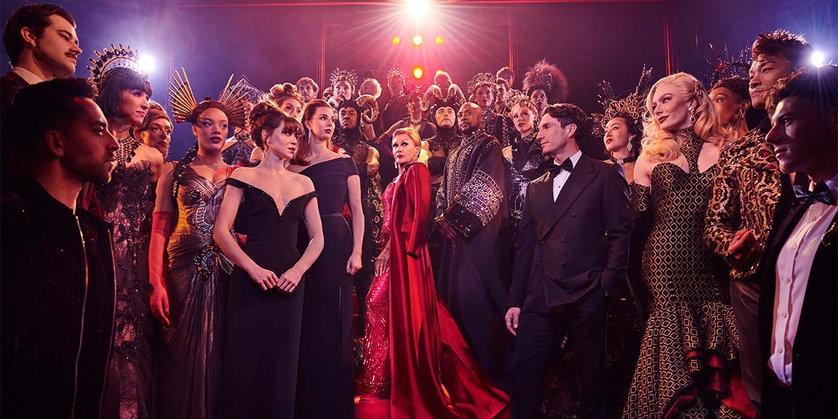 The cast of The Devil Wears Prada poses together, dressed in stylish outfits against a neutral backdrop.