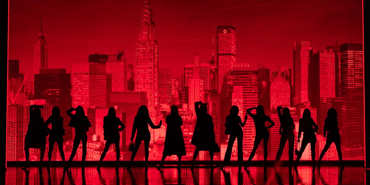 The cast of The Devil Wears Prada poses together, dressed in stylish outfits against a neutral backdrop.