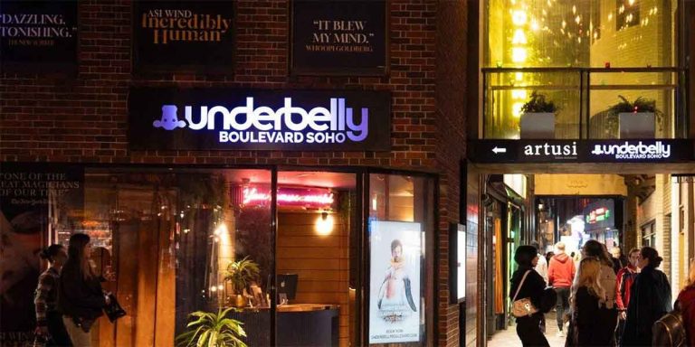 Illuminated sign for Underbelly Boulevard Soho, with people walking past in a vibrant urban setting.