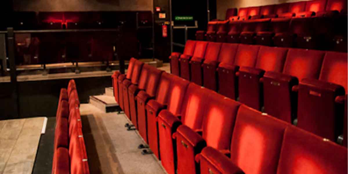 Interior of Jermyn Street Theatre featuring rows of red velvet seats and a wooden stage area.