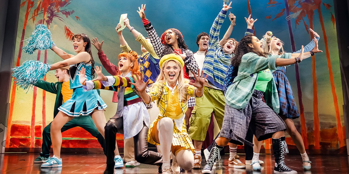 The company of Clueless The Musical are on stage with arms spread out wide, they appear to be happy.
