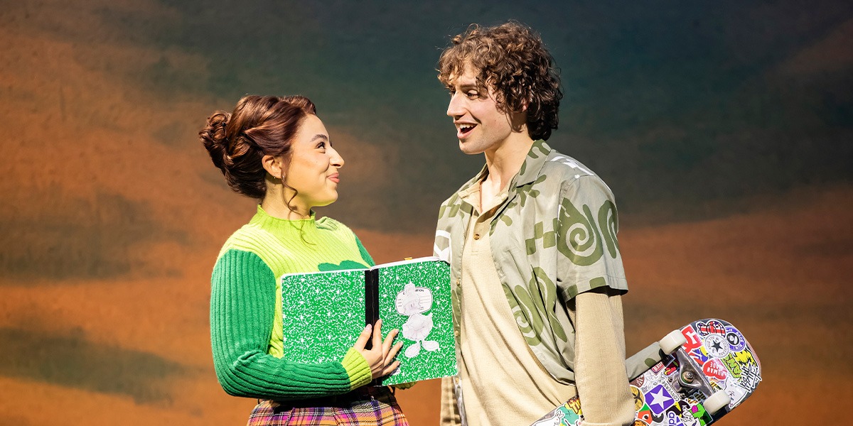 Romona Lewis-Malley (Tai) and Blake Jordan (Travis) are standing smiling at each other.