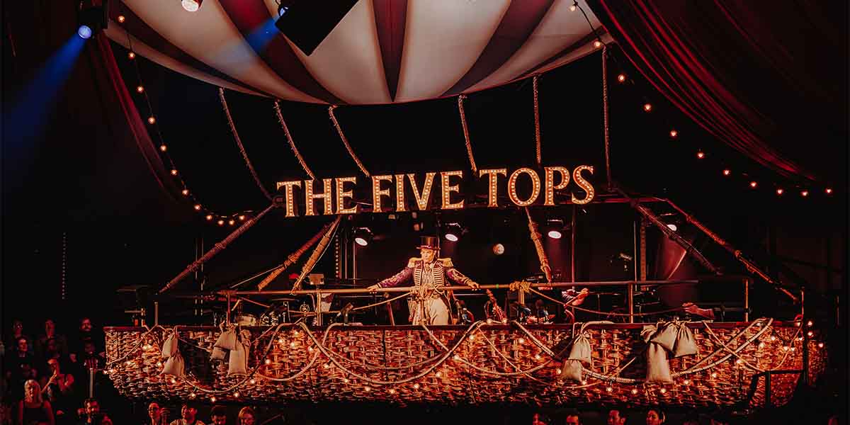 The Five Tops perform on a decorated stage with bright lights, surrounded by an audience in a circus tent.
