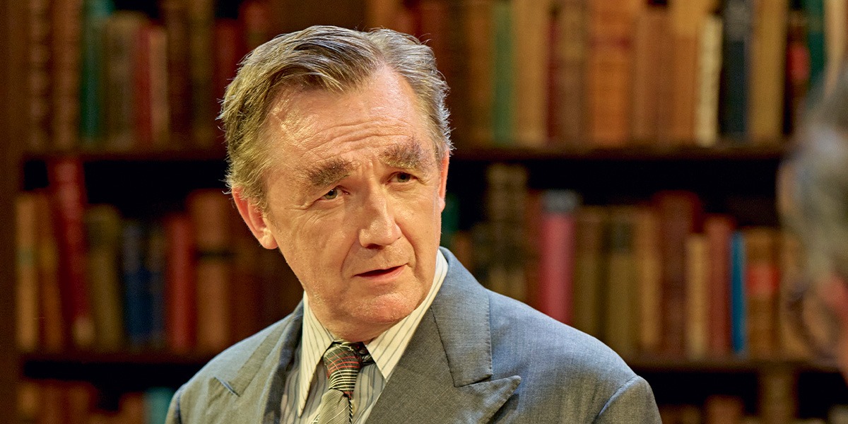 Colin Tierney (Denis Healey) is wearing a grey suit jacket, white shirt and silver tie. Colin Tierney (Denis Healey) appears unpleasantly surprised.