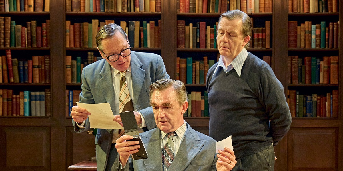 Alan Cox (Tony Crosland) Hywel Morgan (Roy Jenkins ) and Colin Tierney (Denis Healey) are sitting in an office each reading what appears to be a letter. In the background a large, full bookcase can be seen.