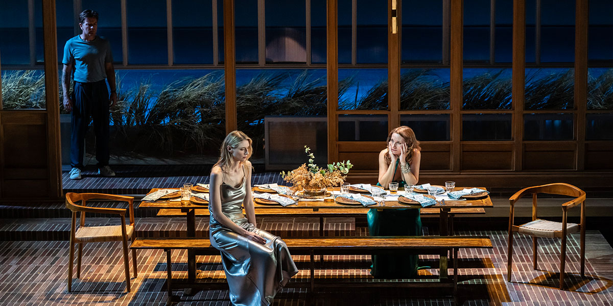 Ewan McGregor, in the dark background, overlooks Elizabeth Debicki Kate Fleetwood who are sat at a dining table