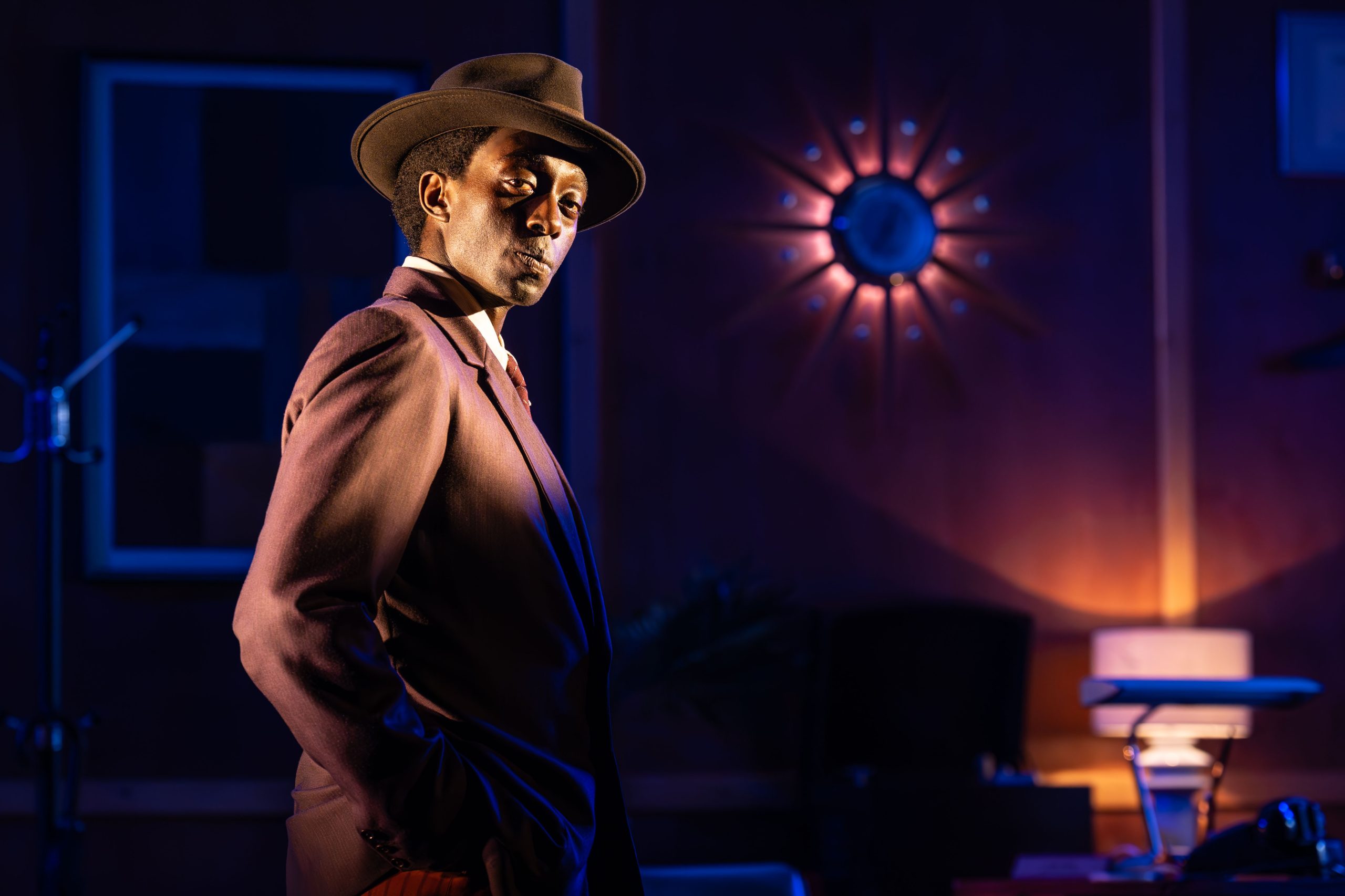 A character wearing a brown hat and jacket stands facing the camera.