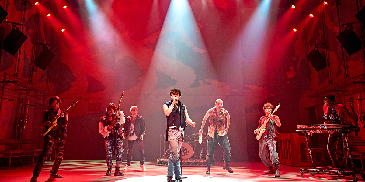 A dynamic stage performance featuring multiple musicians, including vocalists and guitarists, under vibrant stage lighting.