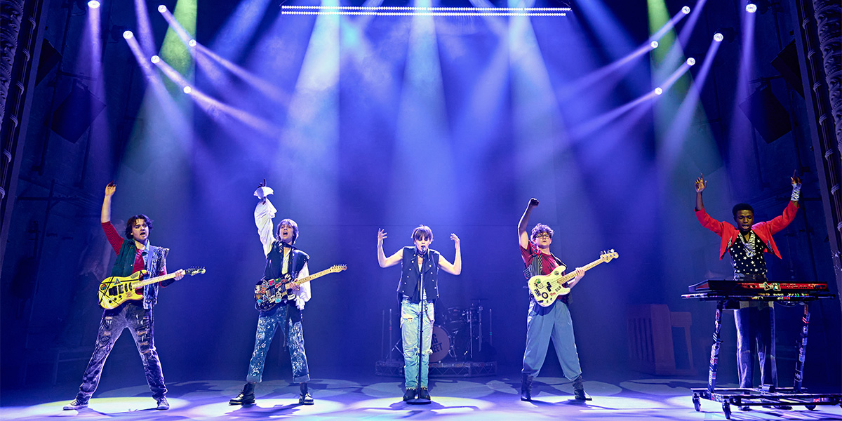 Performers on stage under blue stage lights, with members playing guitars and singing into microphones.