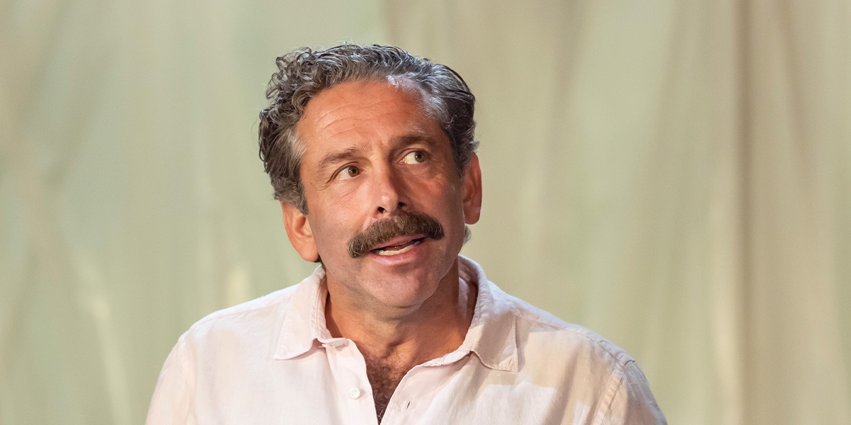 Elliot Levey (Tom Maschler) is looking sideways as if thinking.