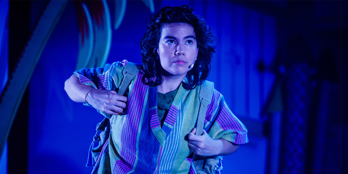 A person stands on stage bathed in warm blue light.