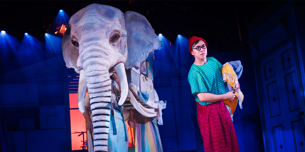 An elephant stands beside a person in colourful costume.