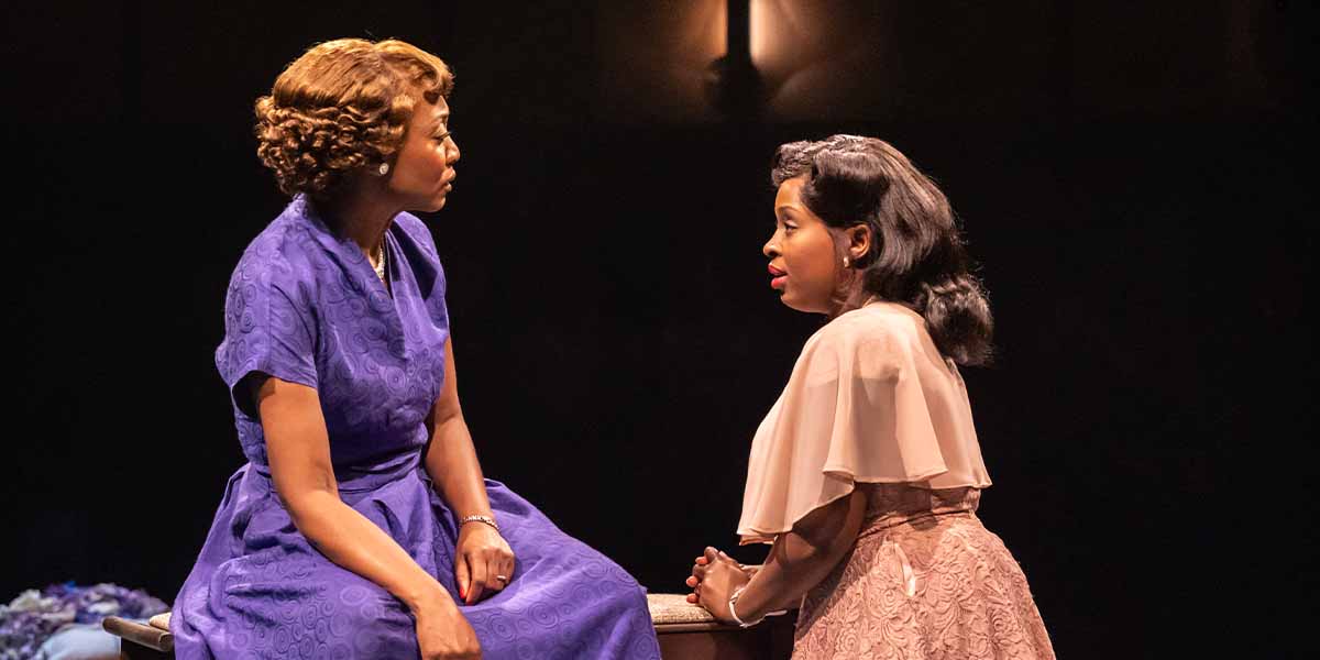 Beverley Knight and Ntombizodwa Ndlovu sit facing each other, engaged in conversation, in a dimly lit setting.