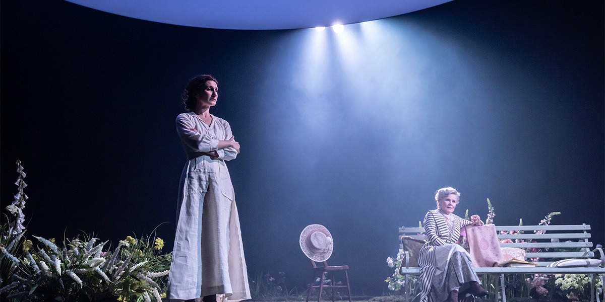 Bessie Carter (Vivie Warren) is standing in the moonlight surrounded by wild flowers while Imelda Staunton (Mrs. Kitty Warren) is seated on a wooden bench behind.