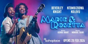 Two women in elegant dresses perform on stage, surrounded by warm lighting and a dark backdrop.