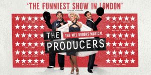 A group of four actors in theatrical costumes, performing on stage with dramatic lighting and a red curtain backdrop.